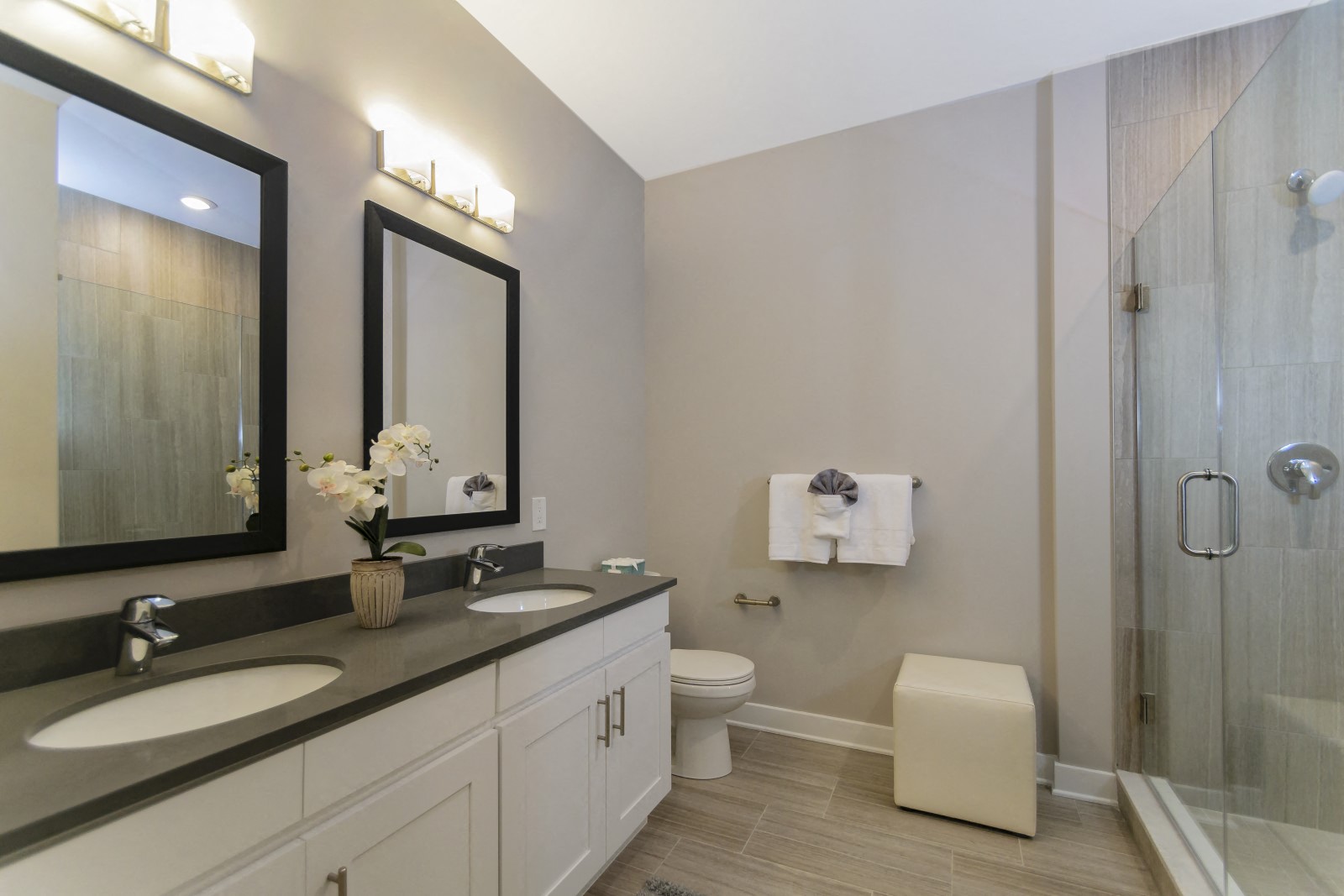 A bathroom with two sink vanities, quartz countertops, two mirrors, a toilet, modern tile flooring, and a stand-up shower. at Keva Flats, Exton, PA