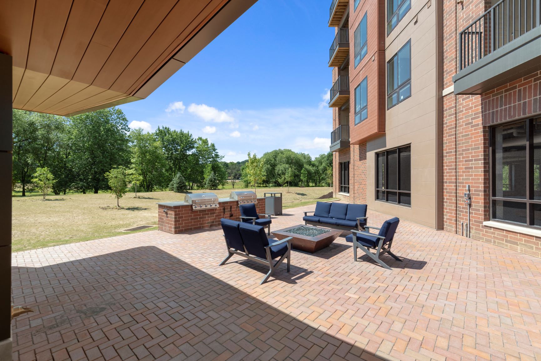 An outdoor fire pit lounge with comfortable seating near a barbecue grilling station and shaded patio  at Keva Flats, Exton, Pennsylvania