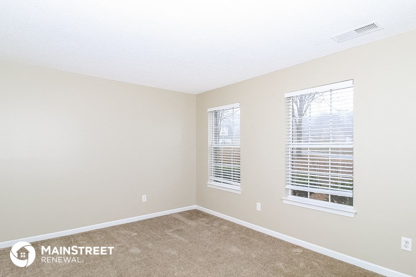 a spacious bedroom with two windows and a carpeted floor