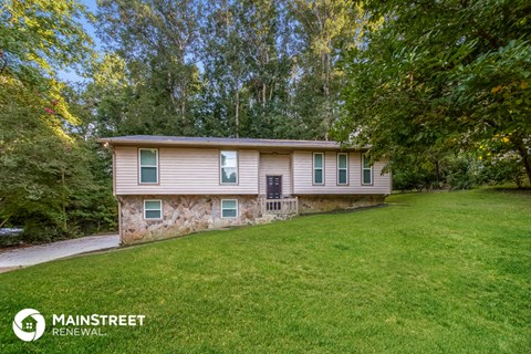 a small tan house with green windows on the side of a lawn