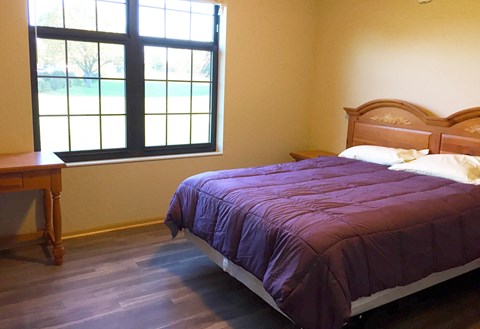 A bed with a purple comforter sits in a room with a window.