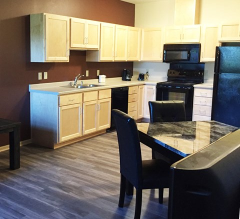 A kitchen with a black refrigerator and a black dining table with four chairs.