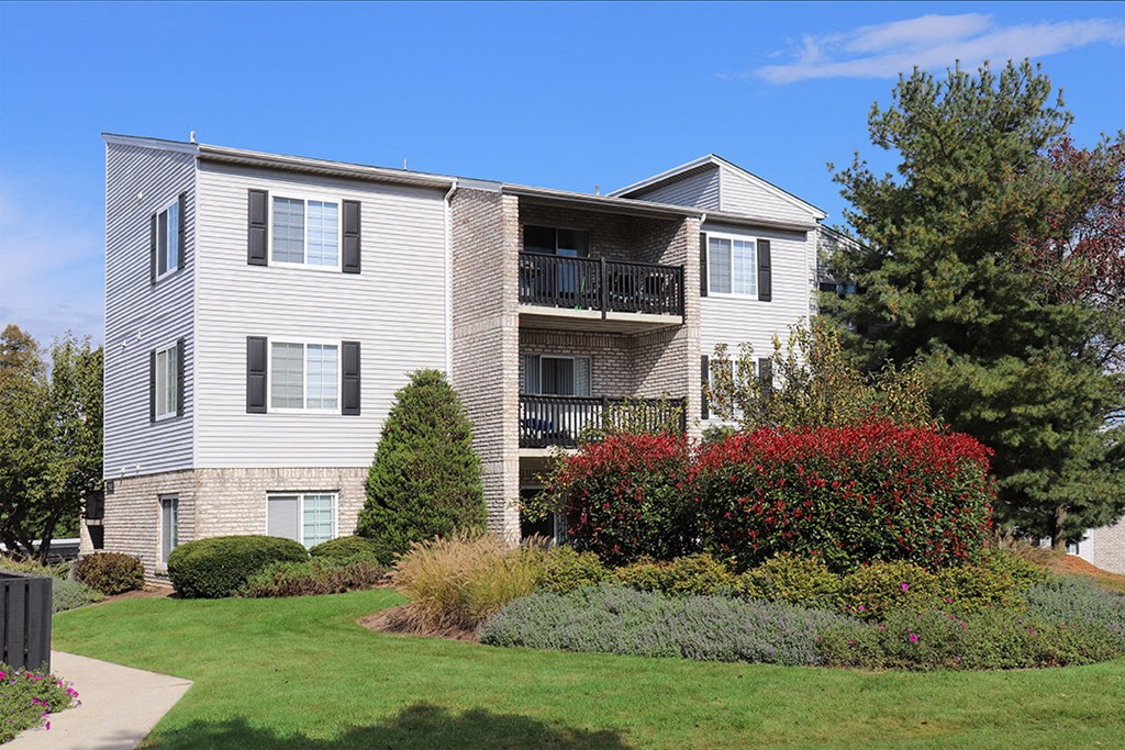 a white apartment building with a lawn and bushes