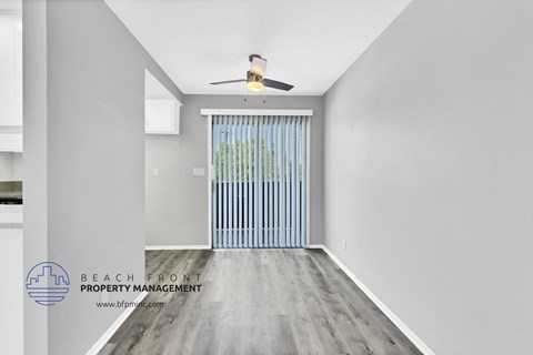 a living room with white walls and wood flooring and a door to a balcony