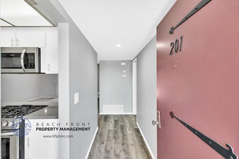 a hallway with a pink wall and a kitchen with white cabinets