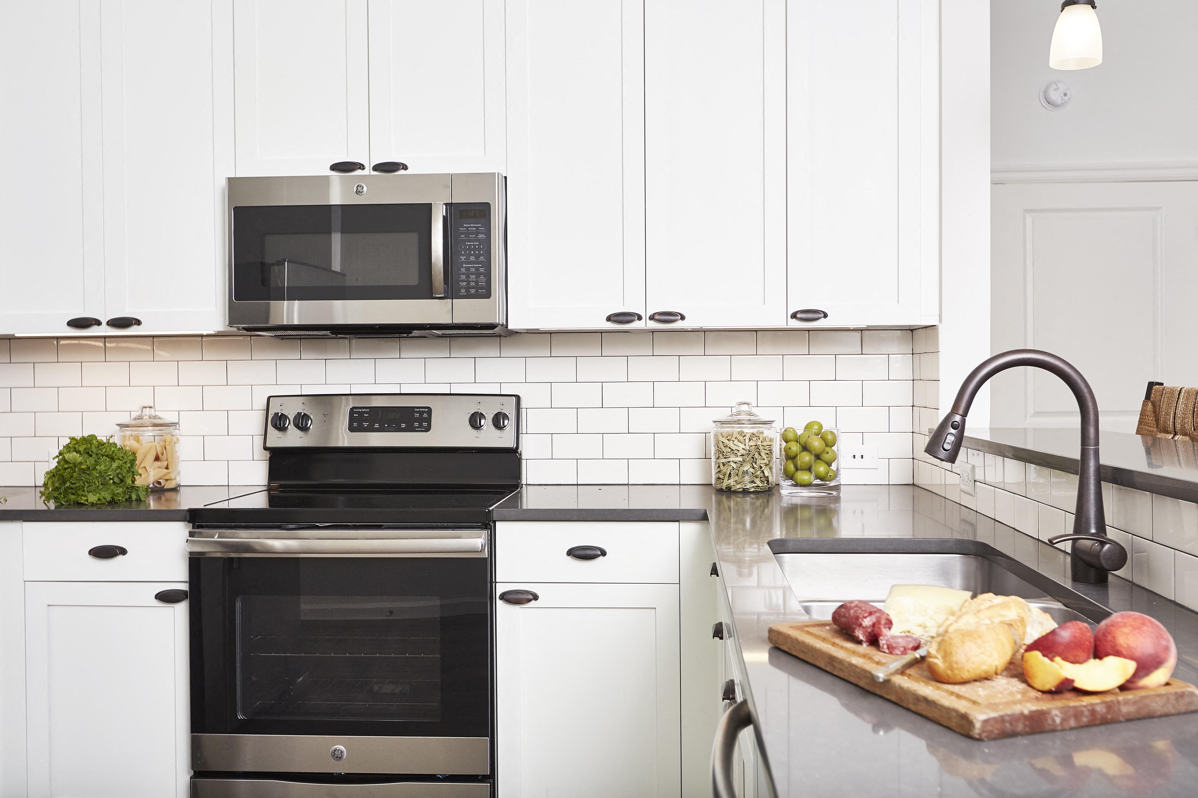A modern kitchen with a black oven and microwave, white cabinets, and a cutting board with fruits and cheese on the counter.