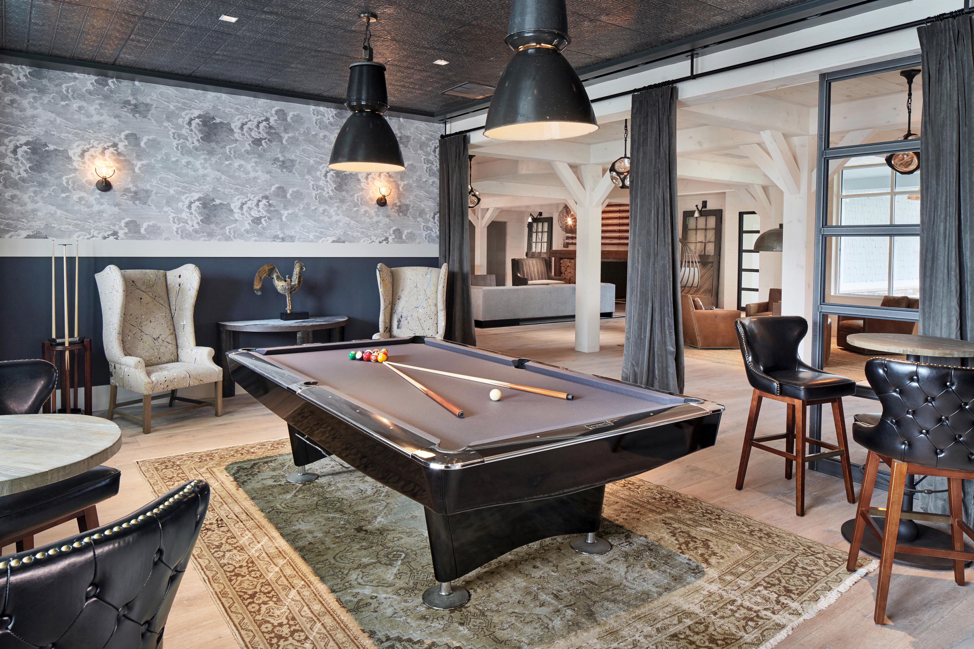 A pool table is in the middle of a room with a black leather chair and a rug.