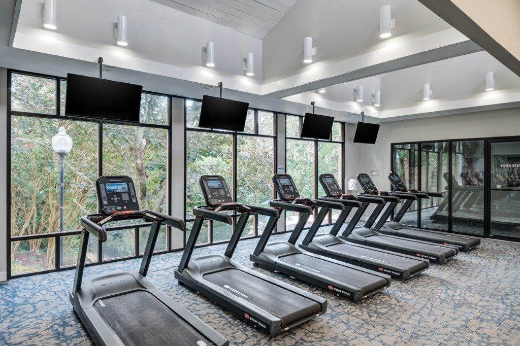 a gym with a row of cardio machines and windows