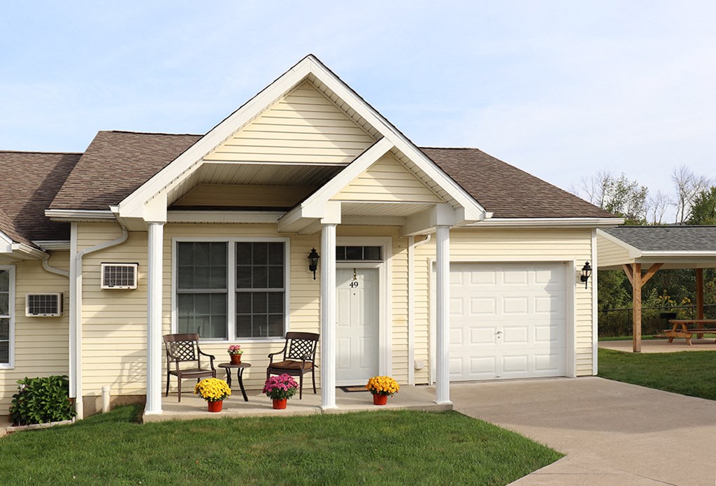 a yellow house with a white garage door and two chairs on the driveway