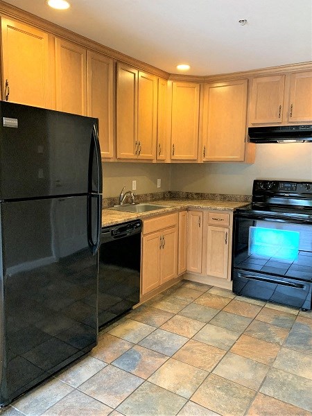 A black refrigerator is in a kitchen with wooden cabinets.