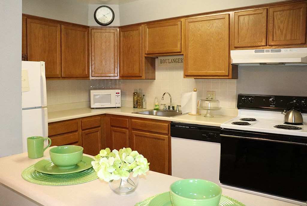 a kitchen with wooden cabinets and white appliances and a table with green bowls and flowers