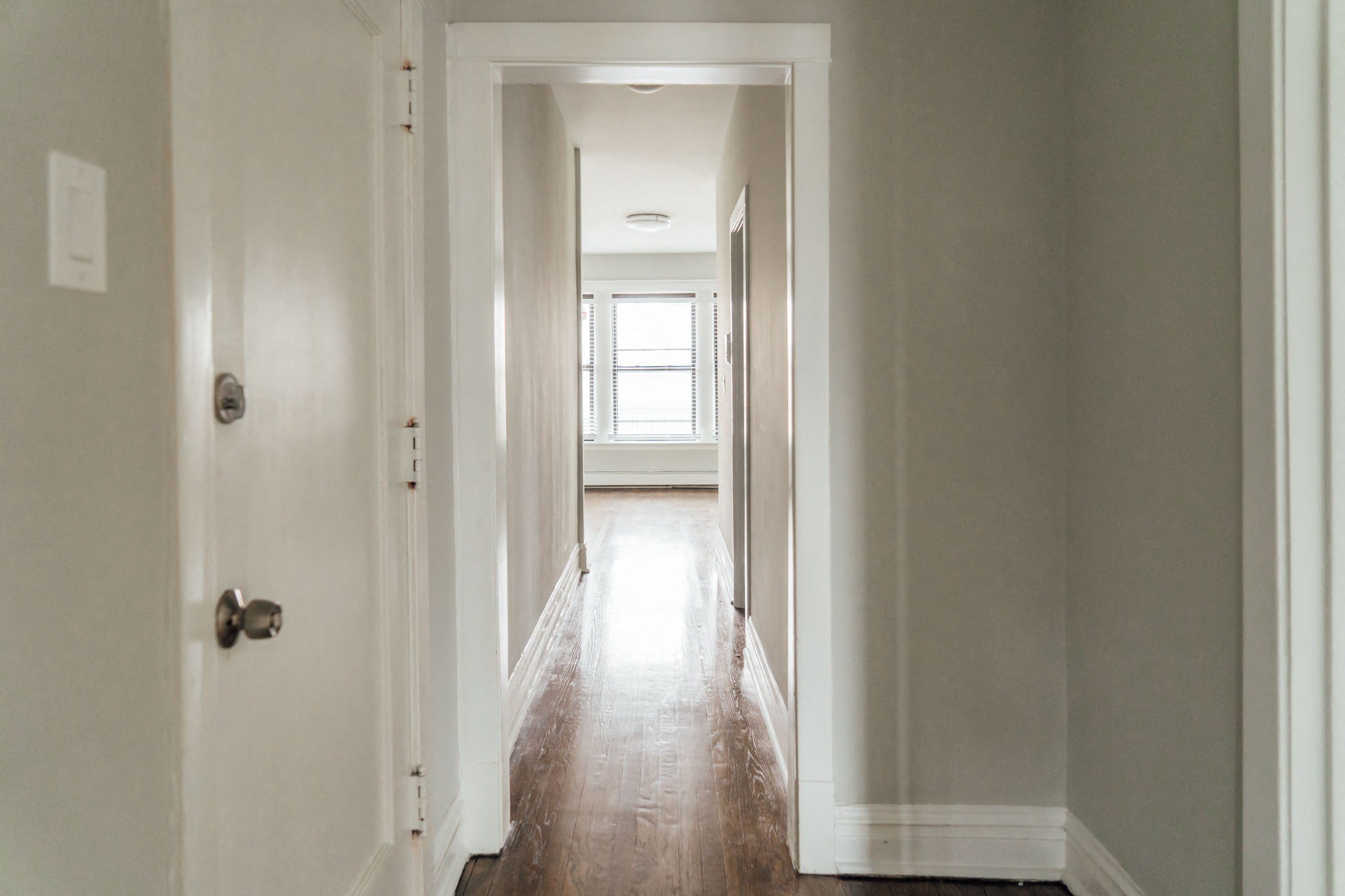 a hallway with white walls and wood floors and a window