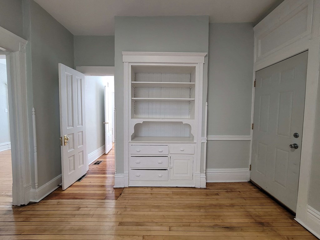 a room with a wooden floor and a white closet with shelves