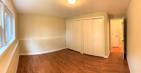 A room with a wooden floor and white walls with a doorway leading to another room.
