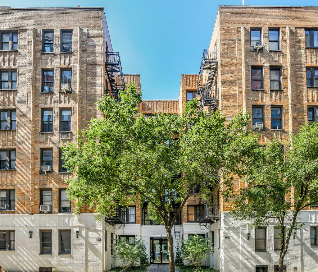 a view of two brick apartment buildings with trees in the middle