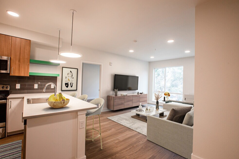 A modern kitchen with a white countertop and a white couch in the living room.