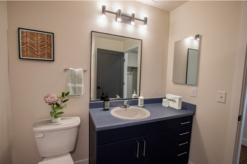 A bathroom with a toilet, sink, mirror, and a vase of flowers.