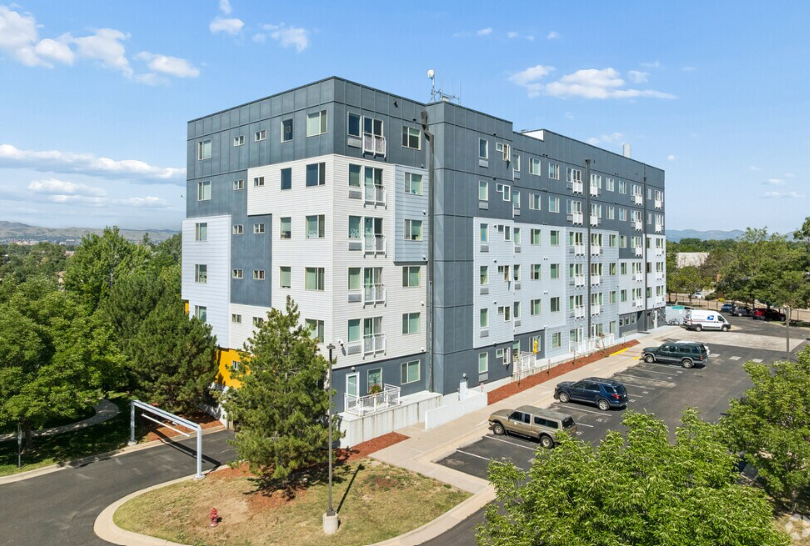 A large grey building with a parking lot in front.