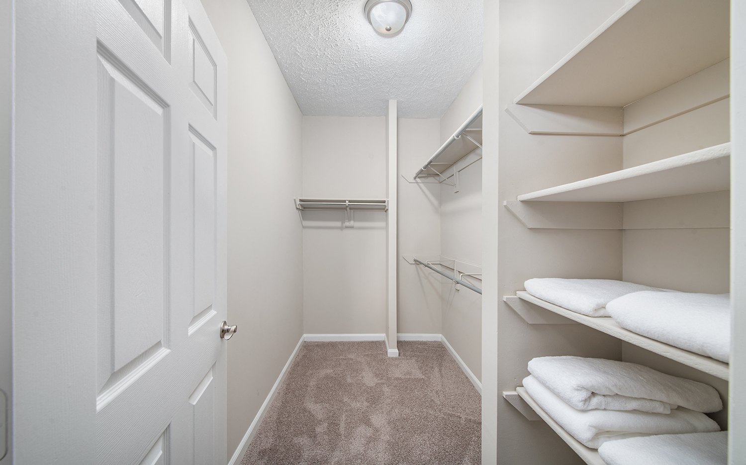 a walk in closet with white closets and shelves and a white door