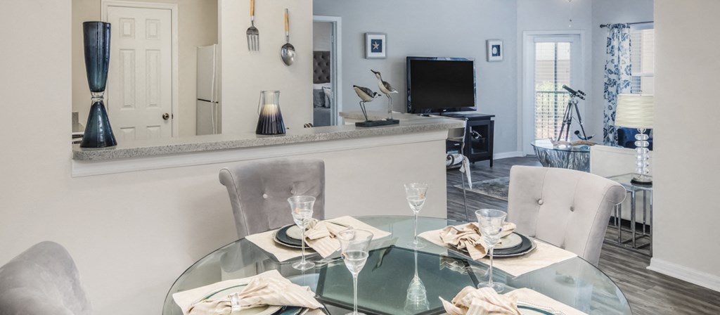 a dining room with a glass table and chairs and a kitchen with a television