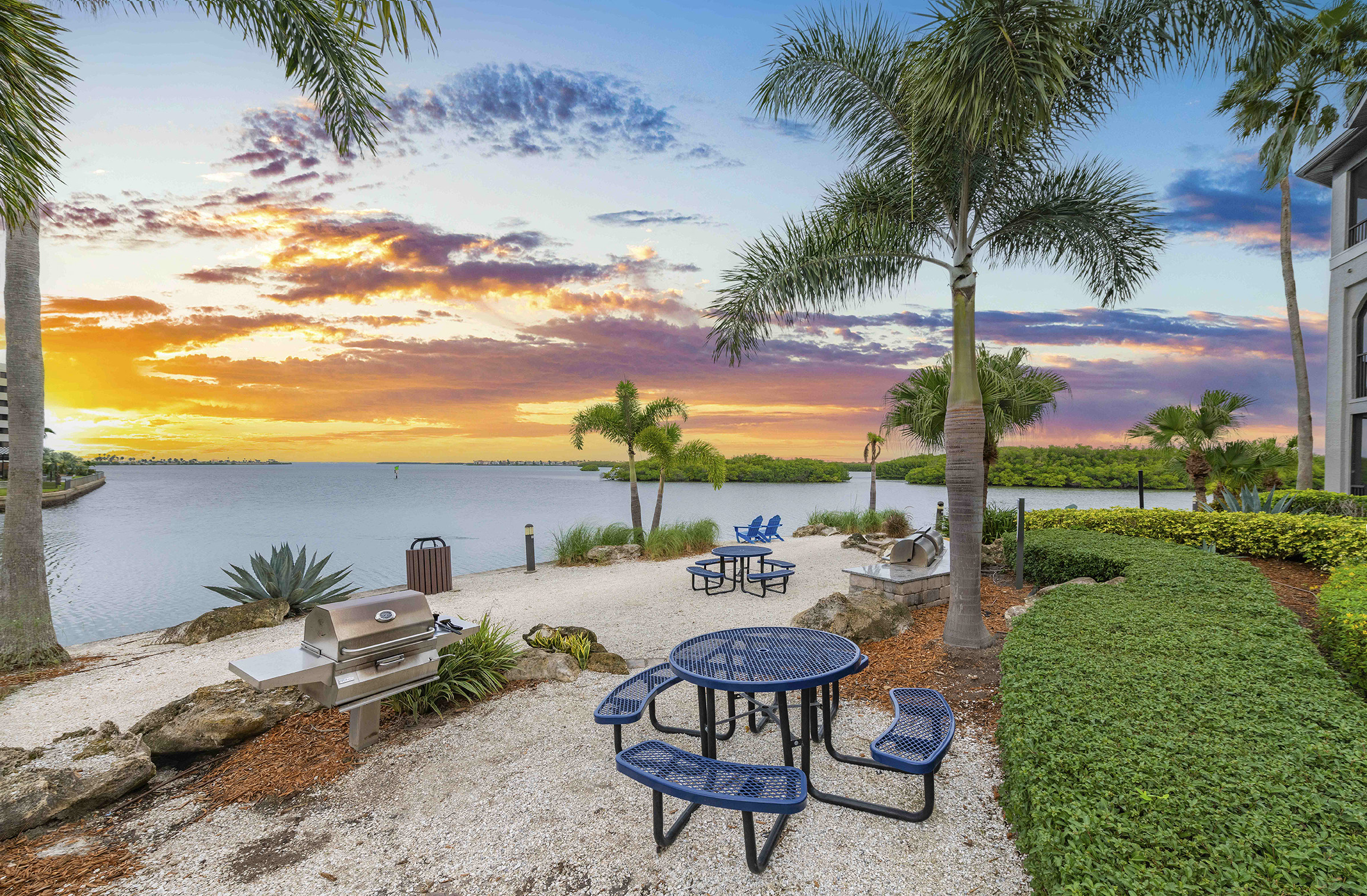 a patio with tables and chairs overlooking the water at sunset