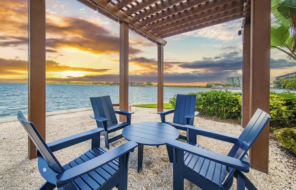 a patio with blue chairs and a table overlooking the water at sunset