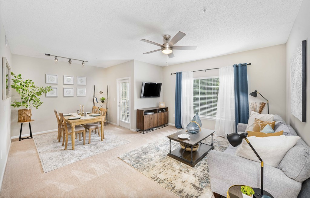 A living room with a grey couch, a wooden dining table, and a ceiling fan.