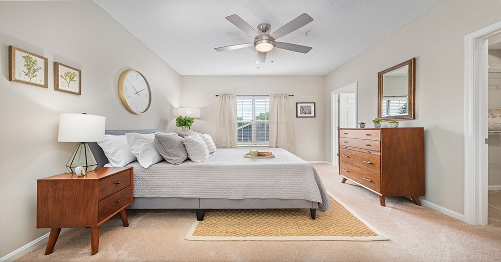 A bedroom with a bed, nightstand, dresser, and mirror.