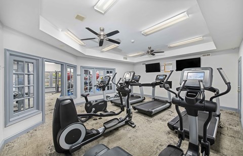 A spacious gym with treadmills, elliptical machines, and a fan.