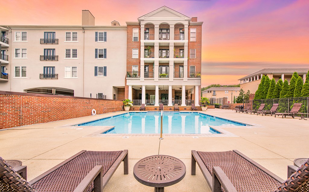 a swimming pool with tables and chairs around it in front of a building