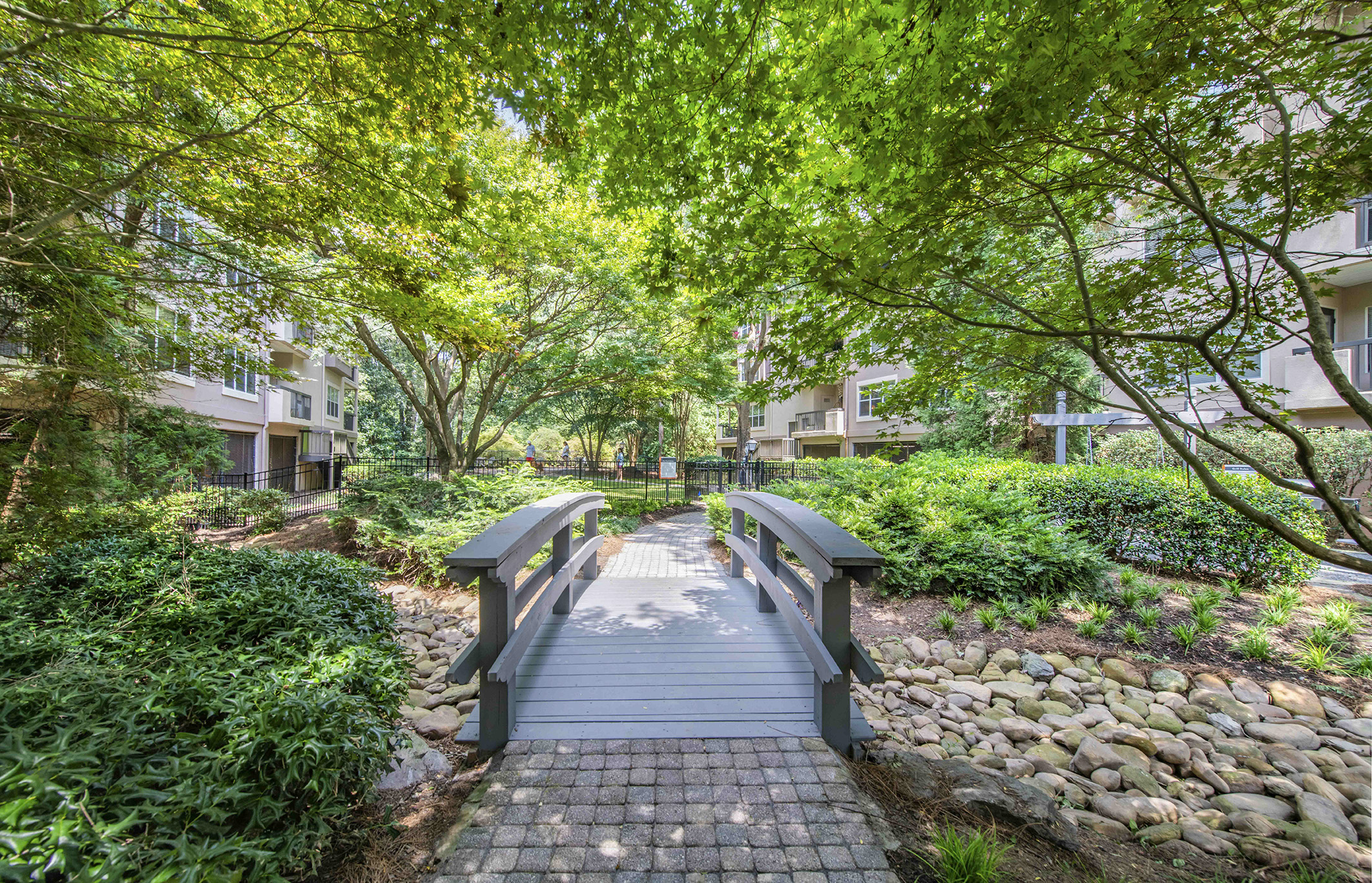 a bridge over a creek in a park with trees and buildings