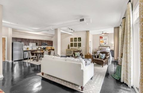 A modern living room with a white sofa and a kitchen in the background.