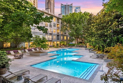 A large outdoor swimming pool surrounded by trees and lounge chairs.