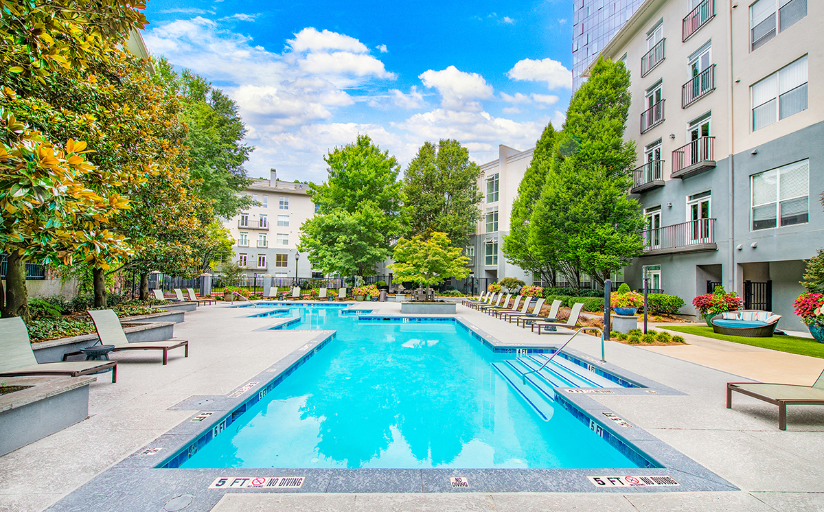 a swimming pool with chairs around it in front of an apartment building