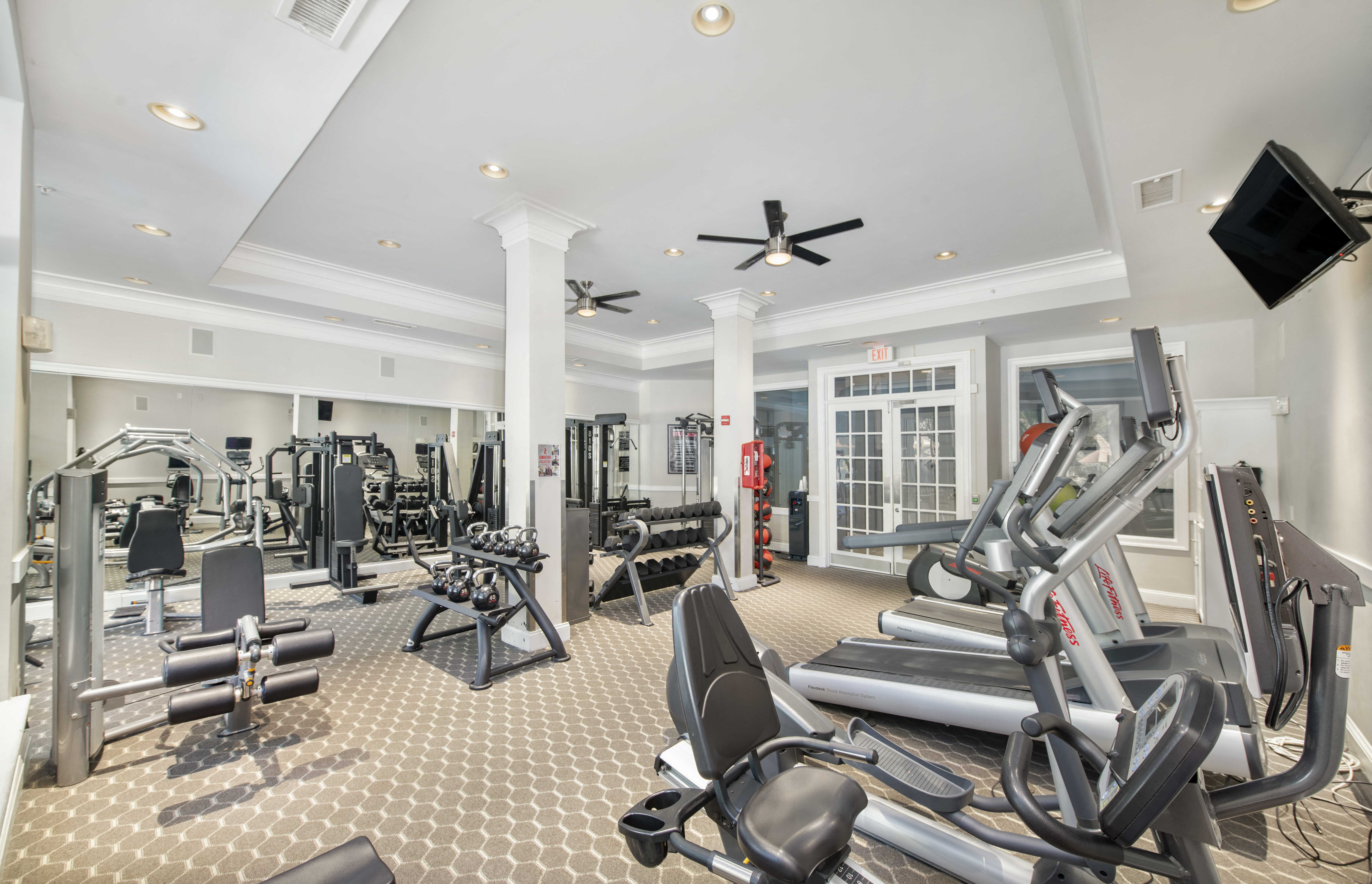 a gym with weights and cardio machines and a ceiling fan