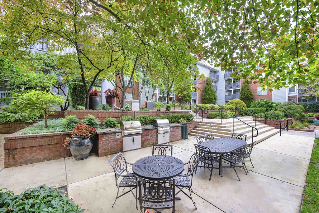 A patio with a table and chairs surrounded by greenery.