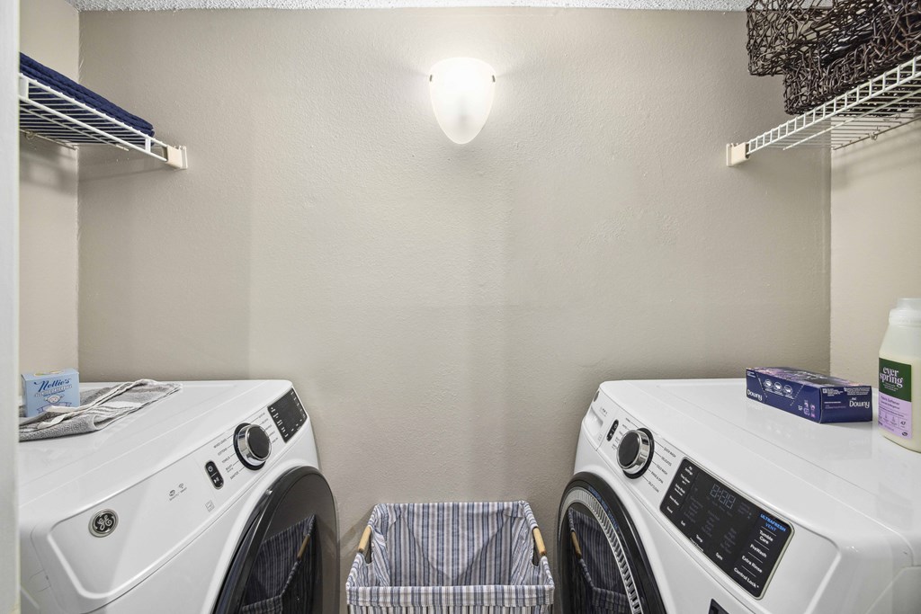A laundry room with two washing machines and a shelf above the dryer.
