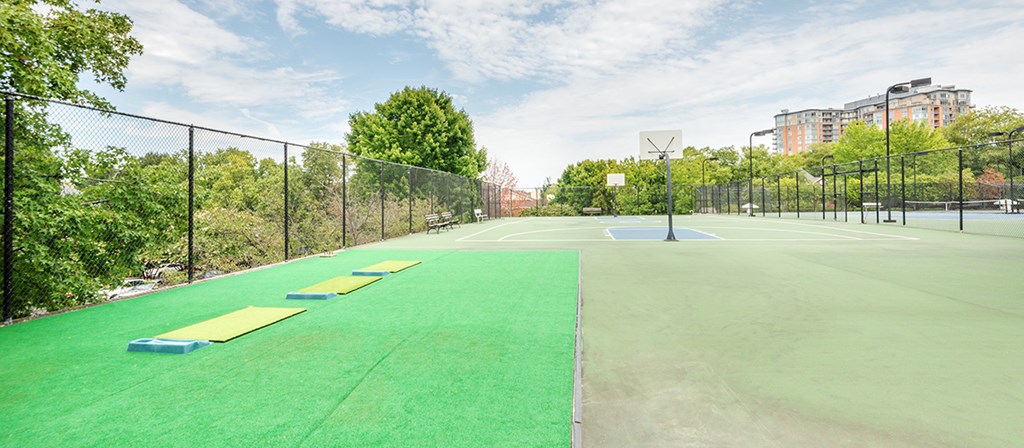 a basketball court on a green field with trees and buildings in the background