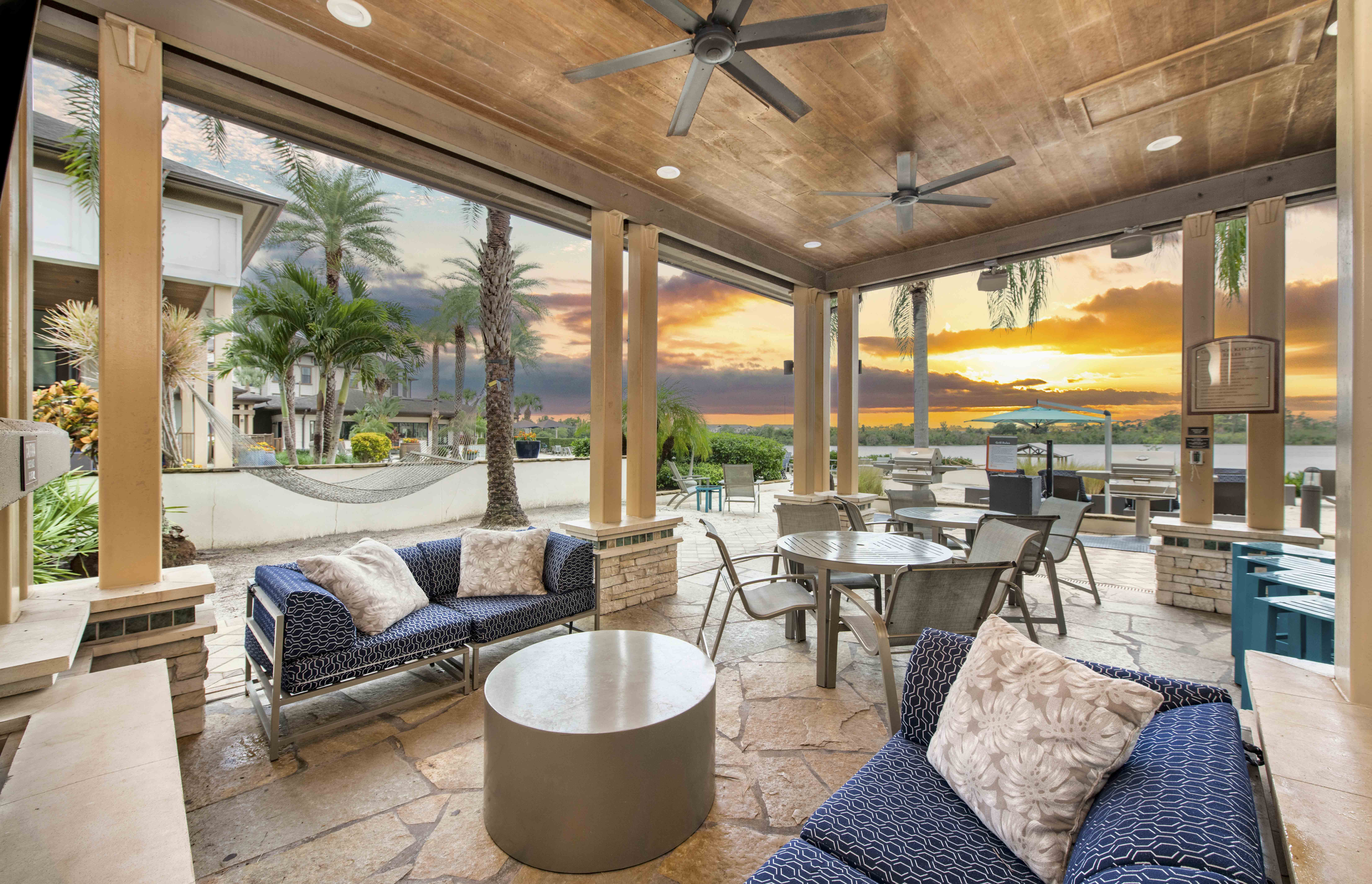 a patio with couches and tables and a sunset in the background