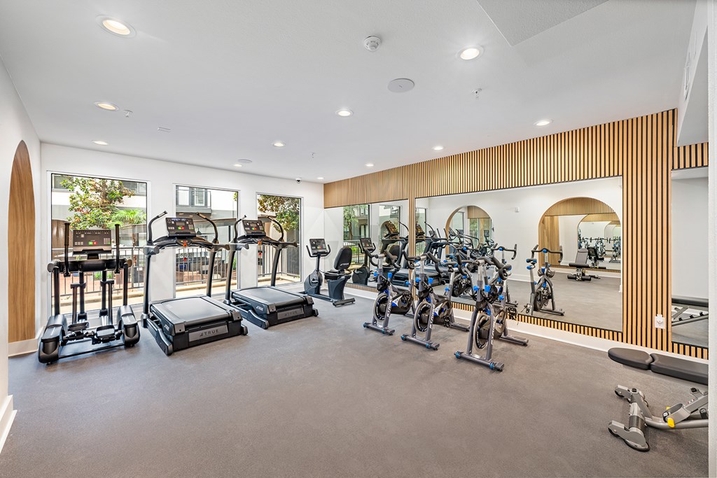 A gym with a variety of exercise equipment including treadmills, stationary bikes, and rowing machines.