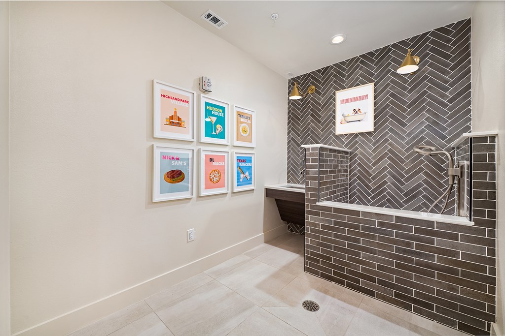 A bathroom with a grey tiled wall and a white wall with pictures on it.