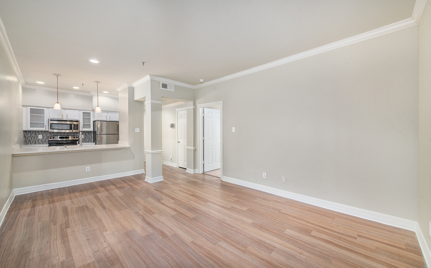 an empty living room with wood flooring and a kitchen