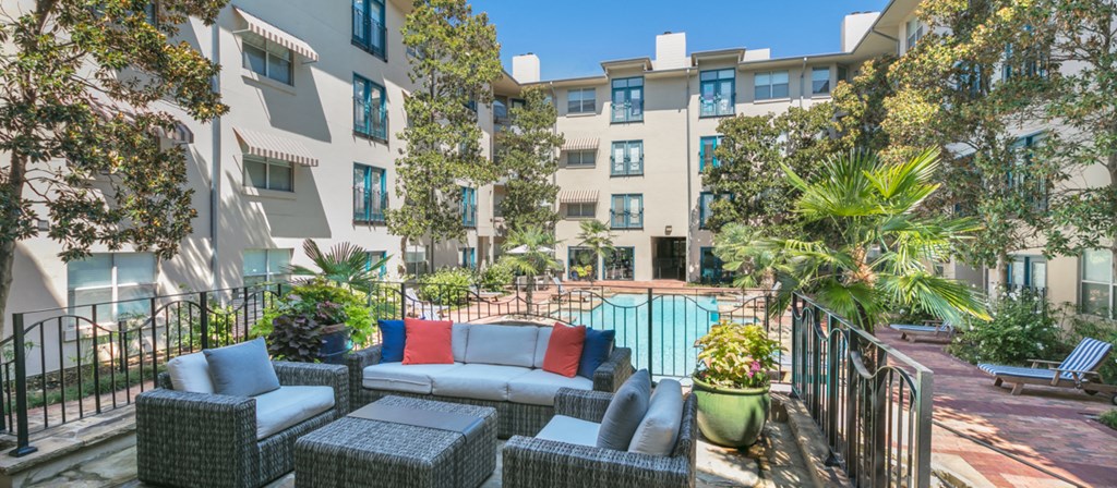 an apartment patio with furniture and a pool in front of an apartment building