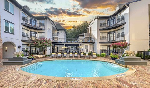 A swimming pool surrounded by a brick patio and lounge chairs.