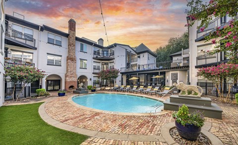 A pool surrounded by a brick patio and a fountain.