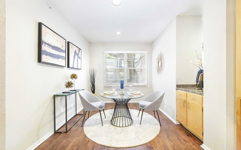 A dining room with a table set for two and a white rug on the floor.