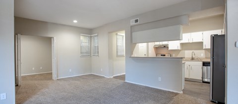 an empty living room and kitchen with a refrigerator and a sink