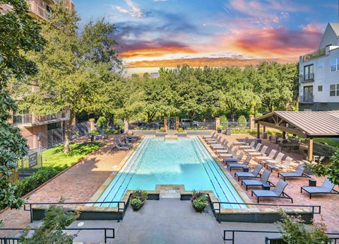 A large outdoor swimming pool surrounded by lounge chairs and trees.