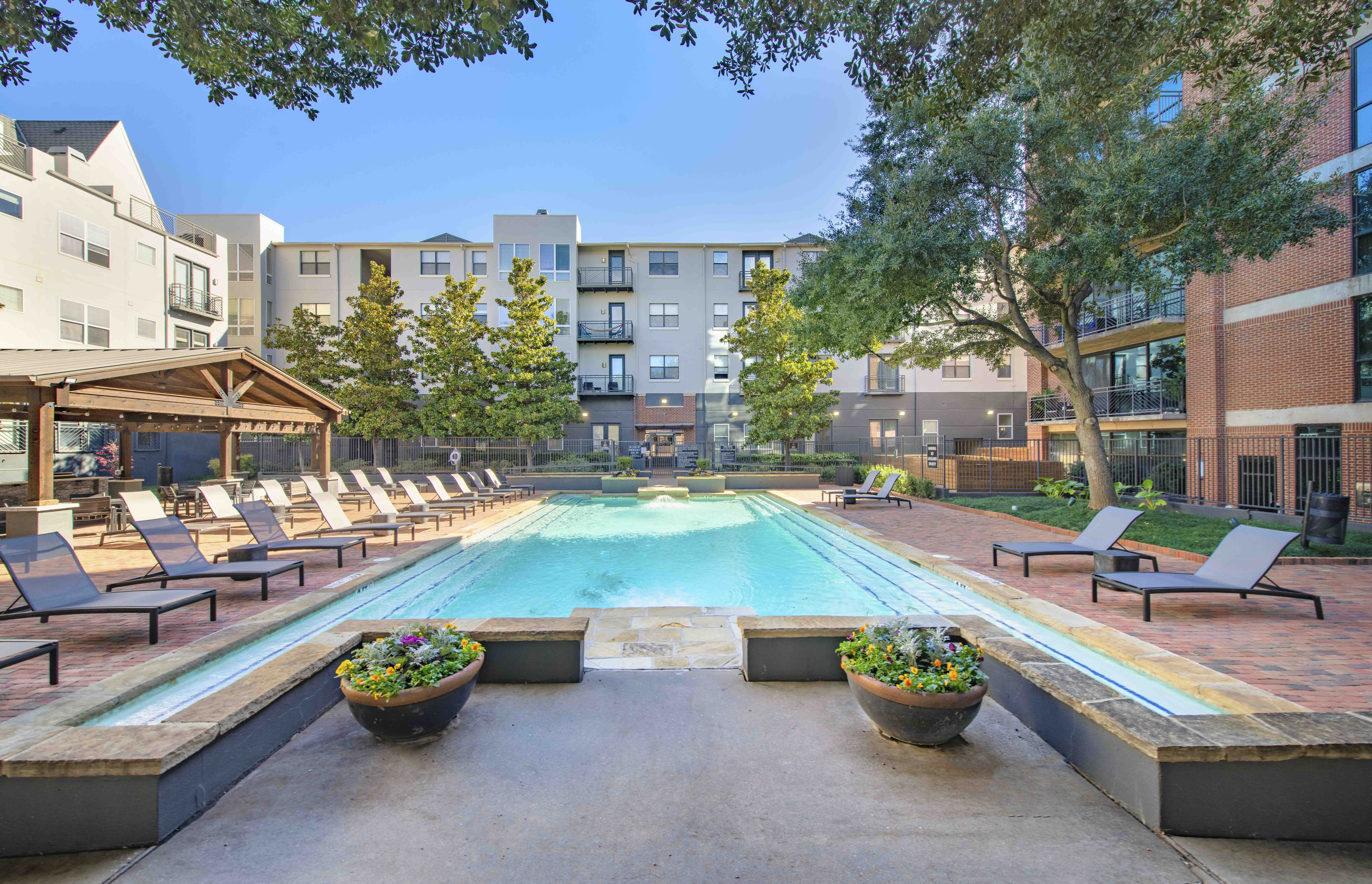 a swimming pool with lounge chairs and trees in front of an apartment building