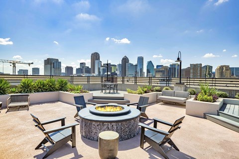 A patio with a fire pit and chairs overlooking a city skyline.